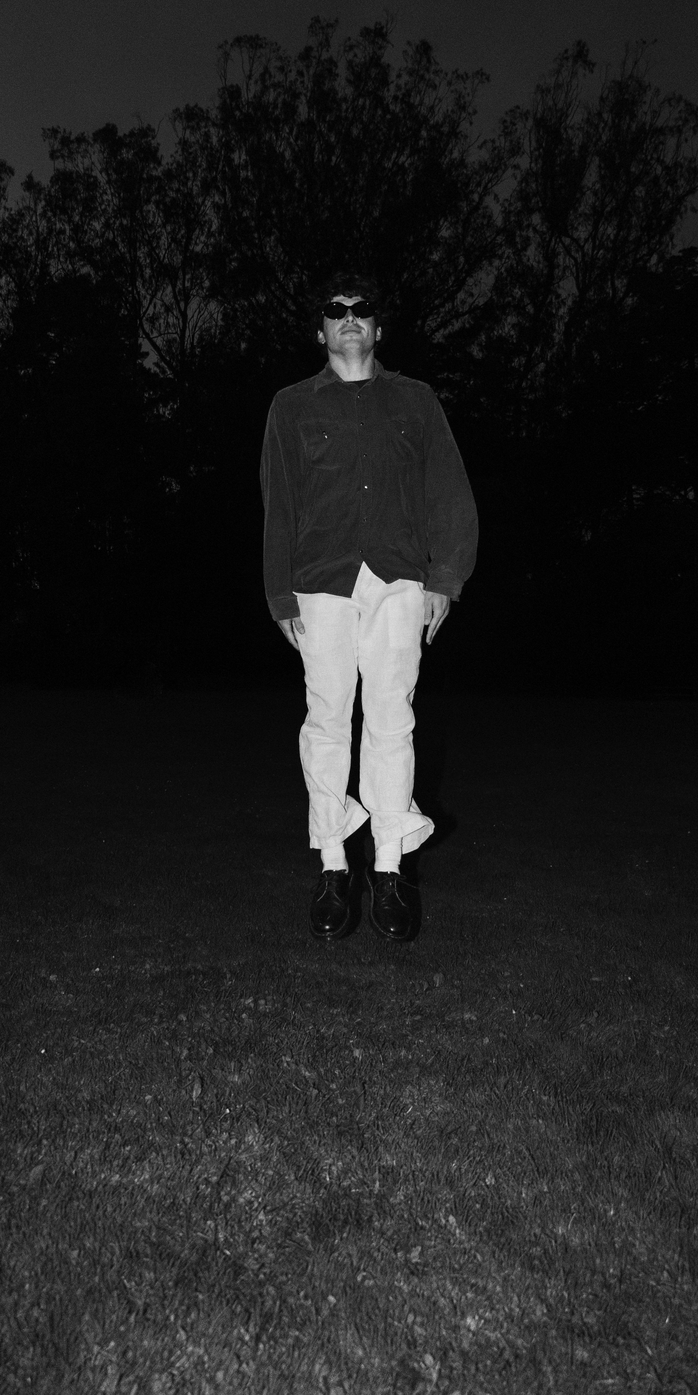 Solitary figure standing in dark field at night, black and white portrait