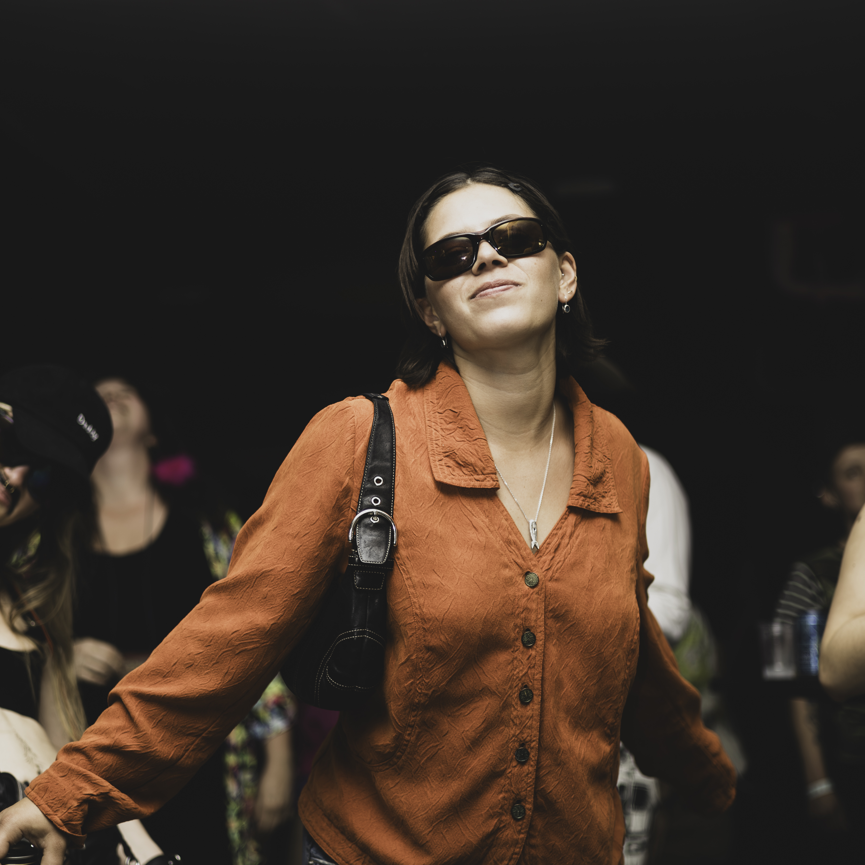 Woman in rust button-up shirt smiling upward, concert crowd, San Francisco