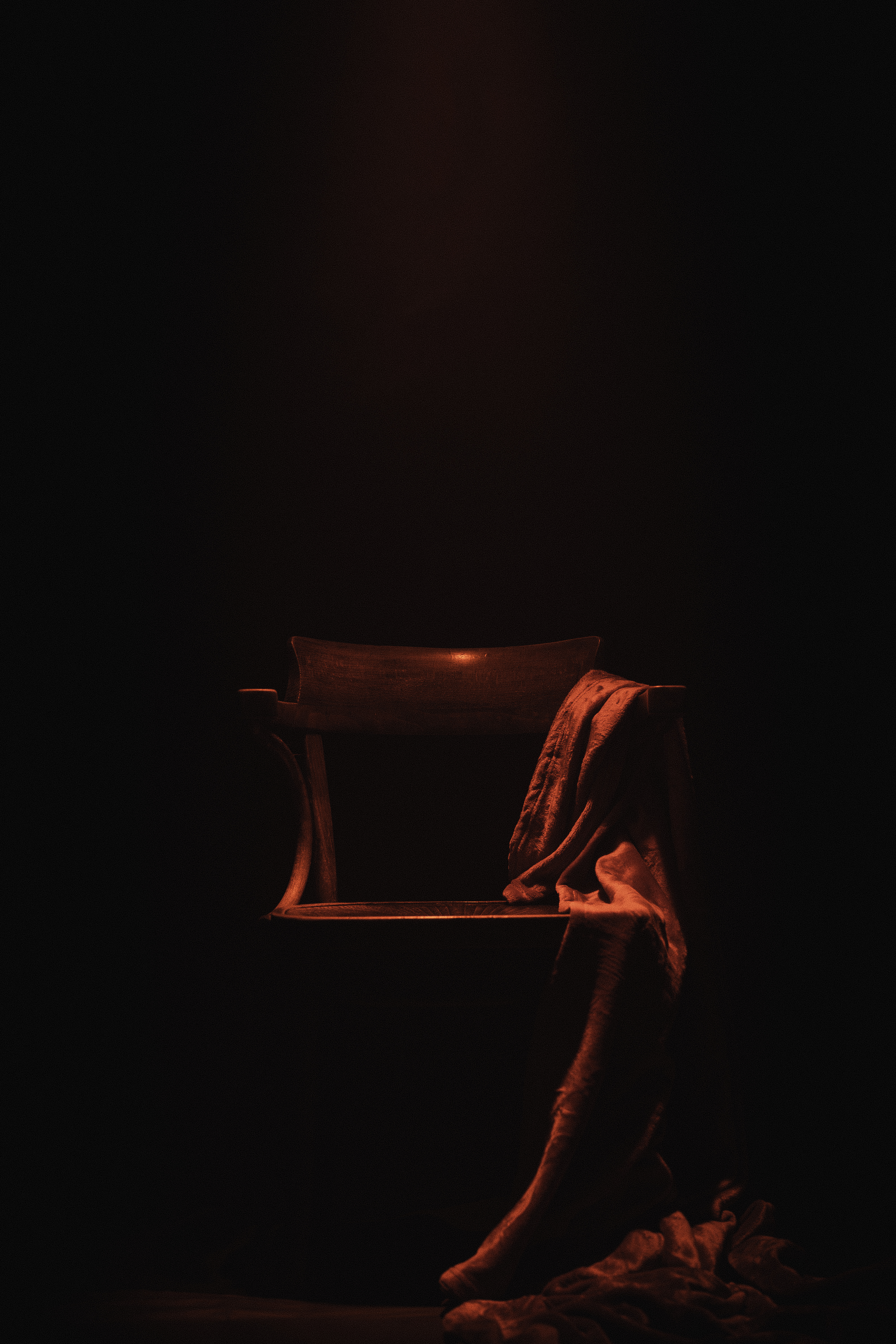 Wooden chair with draped cloth, lit by single warm amber light in darkness