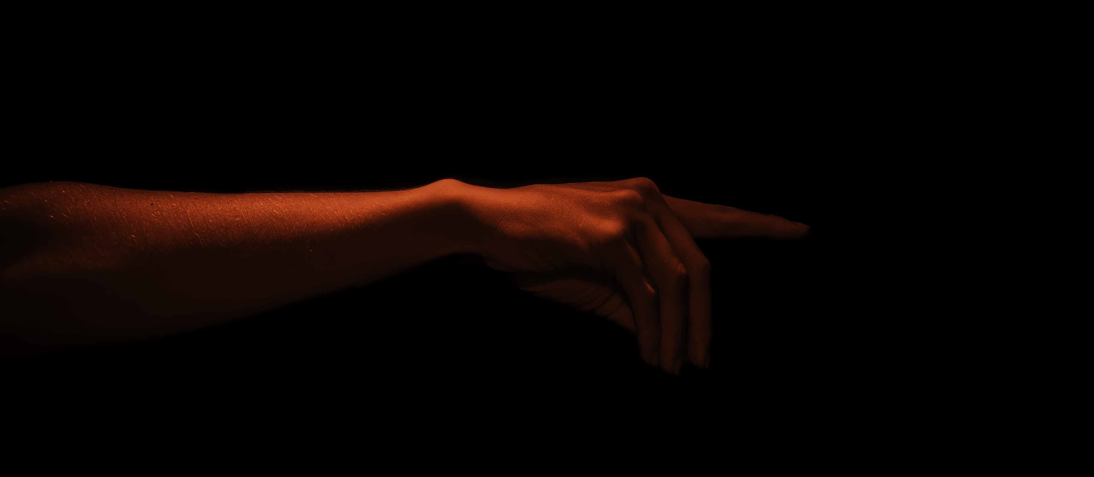 Arm and hand outstretched horizontally against black, deep red studio light