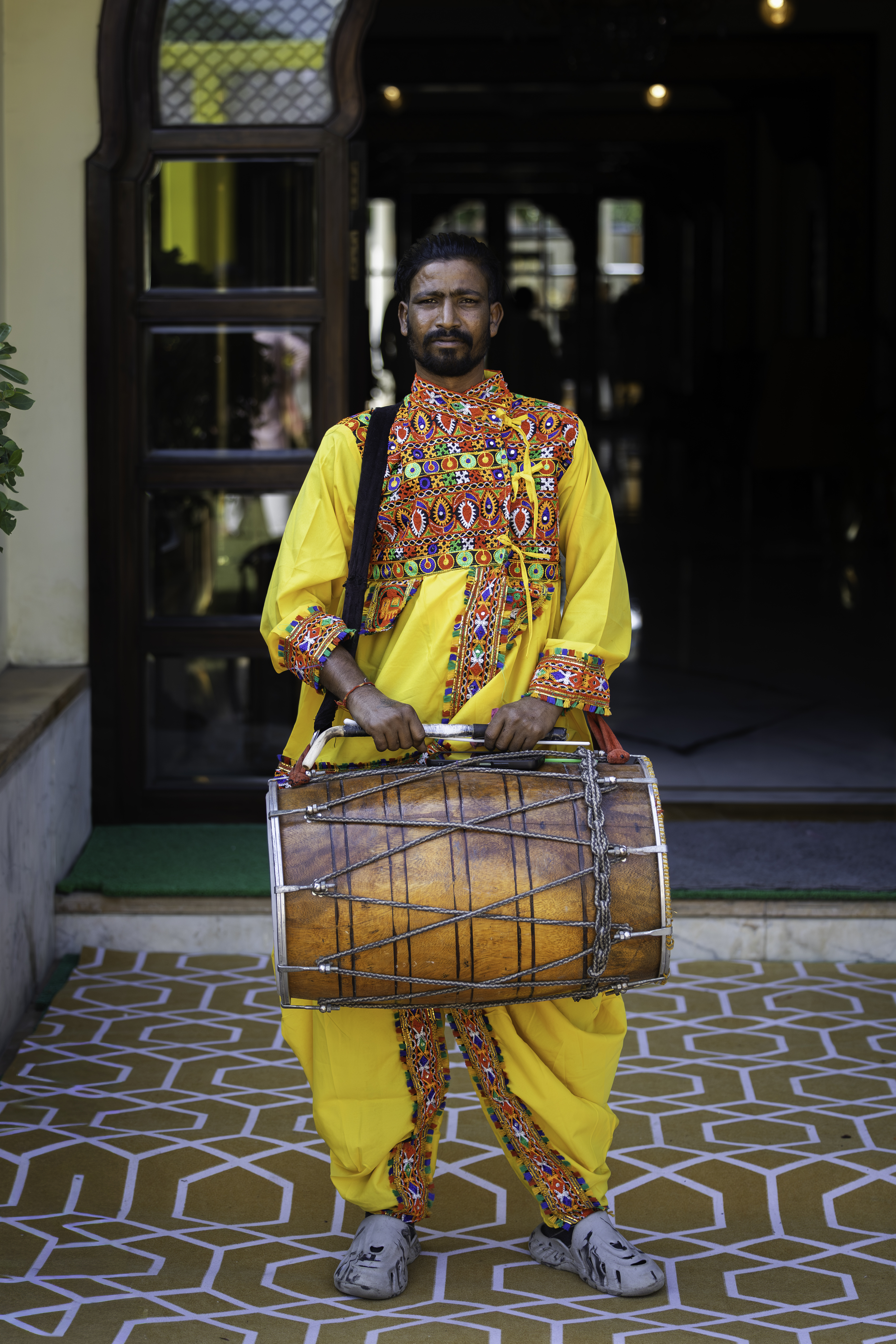 Man in traditional yellow Rajasthani embroidered outfit holding a dhol drum